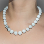 A set of pearls are carved from white erasers then knotted and strung onto silk. Some pearls have black marks from pencil lead on them. Photographed on the body with a grey background.
