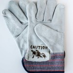 A pair of brand new leather work gloves are branded with the Immigrant Crossing Sign and photographed on at white background.